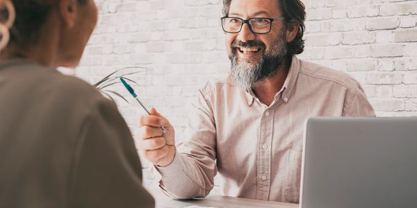Man with glasses smiling and holding a pen during a discussion.