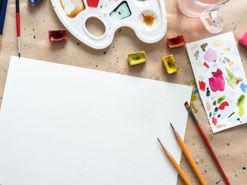 Artist's workspace with blank paper, paint palette, brushes, and watercolor paint.