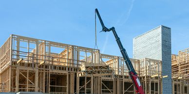 Crane lifting wooden frames at a building construction site under clear blue sky.