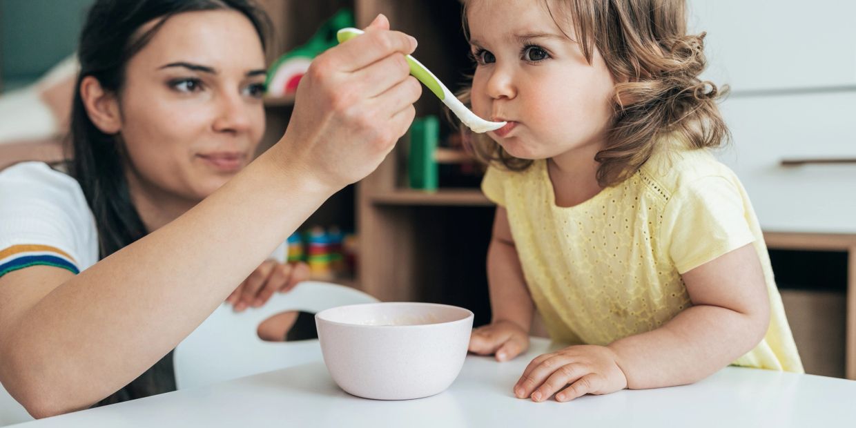 Mother feeding her young daughter with a spoon.