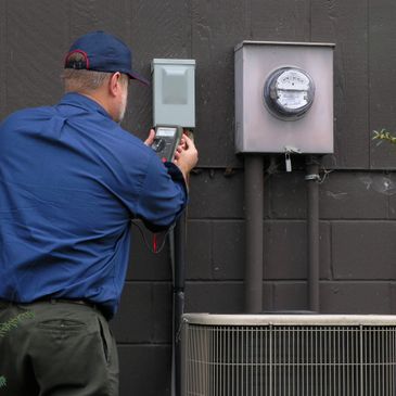 Technician inspecting an electric meter outside a building.