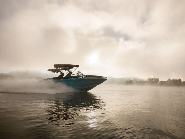 A blue speedboat cutting through misty waters at dawn.