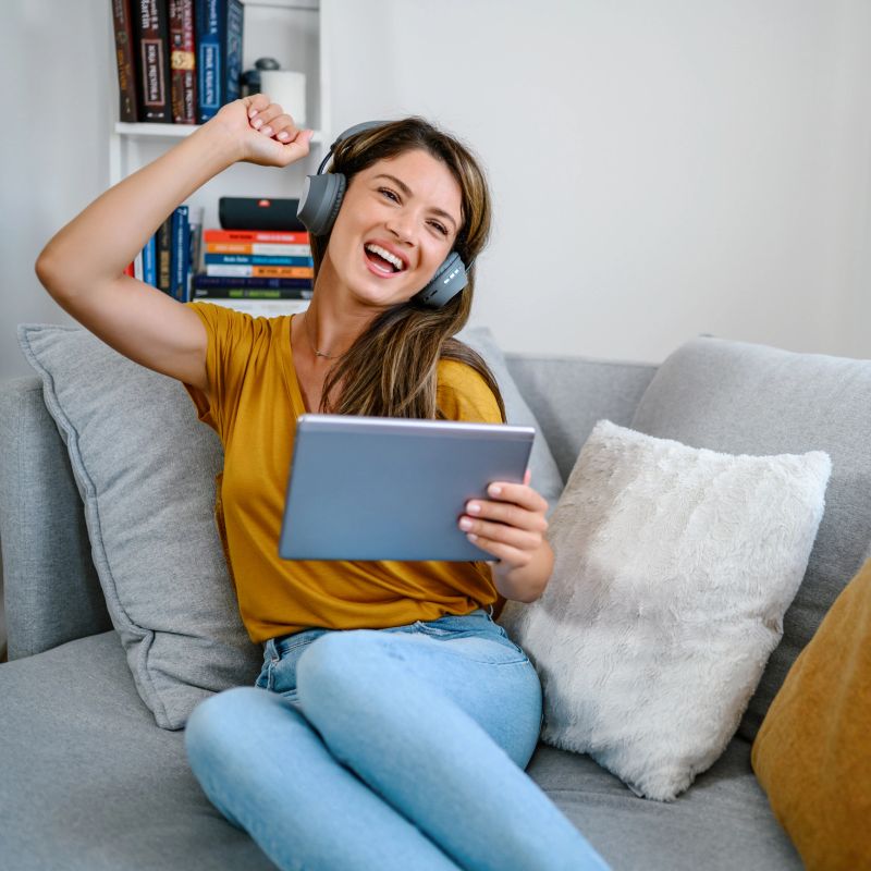 Woman using tablet for watching online movie stream mobile device on sofa at living room. Young happy girl enjoying with entertainment media online on weekend.