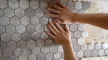 Hands installing hexagonal floor tiles on a surface.