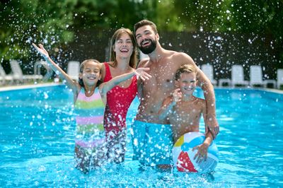 Smiling family enjoying a clean backyard pool on a sunny day, showcasing Bright Bottom Pools