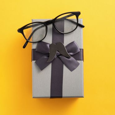 Gift box with a mustache pin and glasses on a yellow background.
