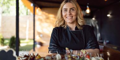 Smiling female chef standing in front of a table with food.