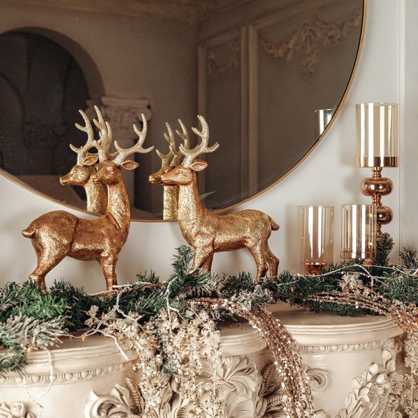 Fireplace mantle with gold reindeer, candle holders and green garland with gold sprays.
