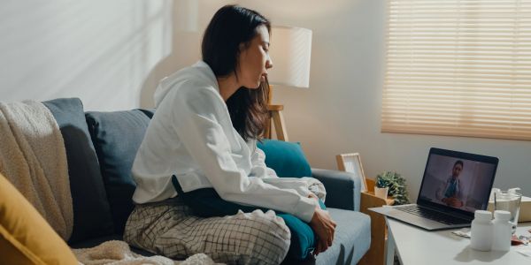 Woman sitting on a couch engaged in therapy over a video call on her laptop.