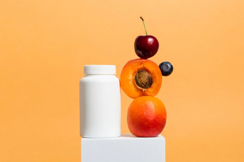 Multivitamin bottle of vitamins or pills with fresh fruits on orange background, bio supplement, organic medication