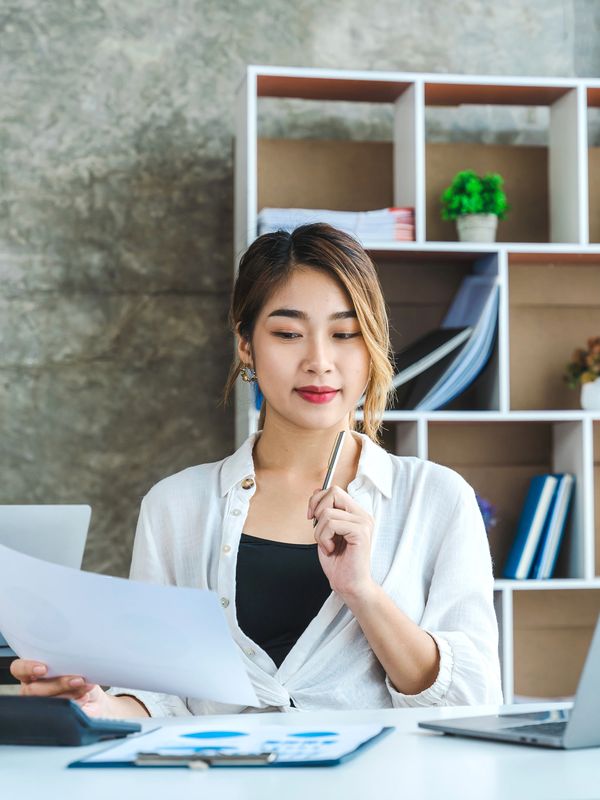Young woman reviewing documents at her desk with a laptop and office supplies.