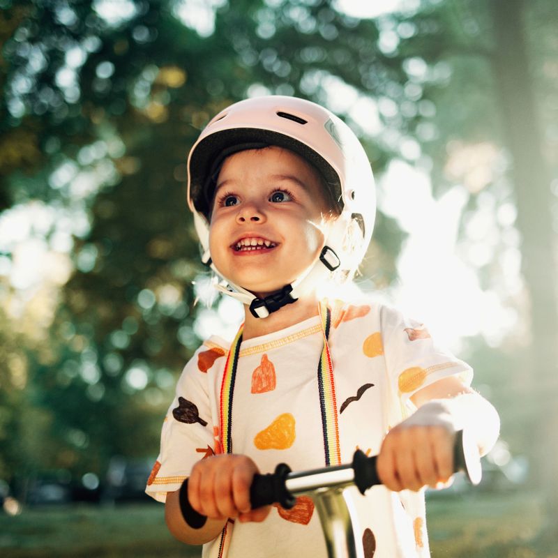 Portrait of an adorable girl riding a scooter in the park on a sunny day. She is wearing a protective white helmet. She is excited and happy.