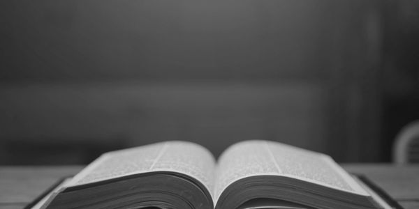 Black and white photo of an open book on a wooden table.