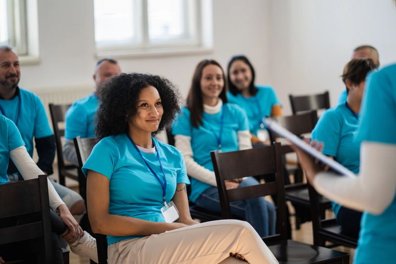 Listening to a seminar a diverse group of people in matching t-shirts and lanyards are sitting and learning about humanitarian aid