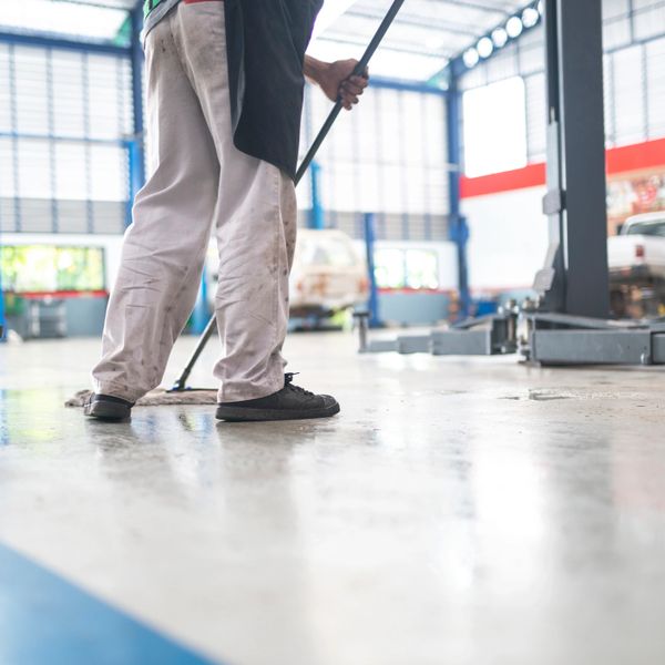 Person mopping floor in a bright, spacious garage or workshop.