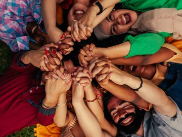 Group of diverse friends lying in a circle holding hands and smiling.
