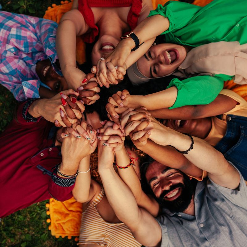 A group of reunited friends are lying on the grass in the park in a circle holding their hands together after Covid19 lockdowns