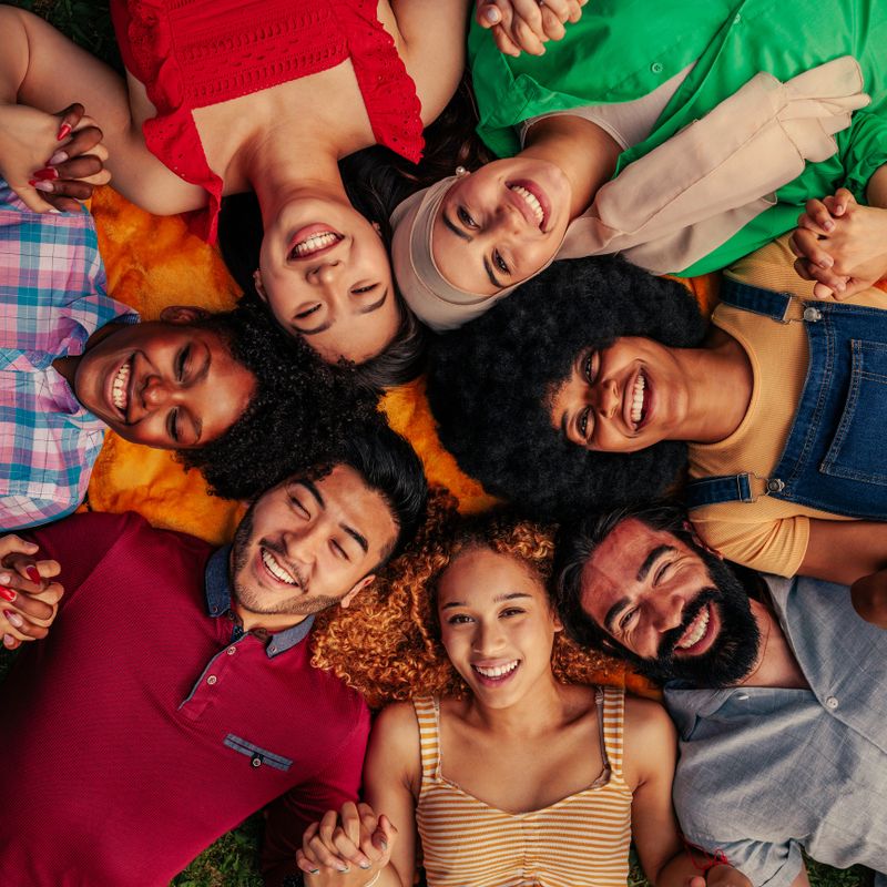 Diverse group of young adults representing unity, friendship, teamwork and community lying on the grass in a circle