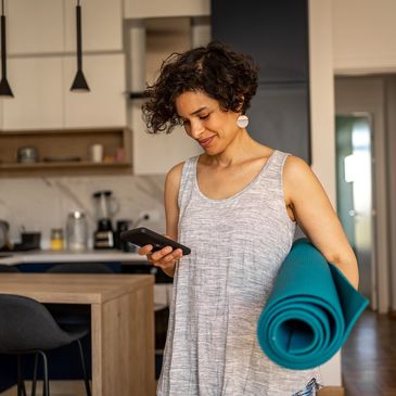 Woman holding a yoga mat, checking her phone, relaxed and ready for a calming wellness session.