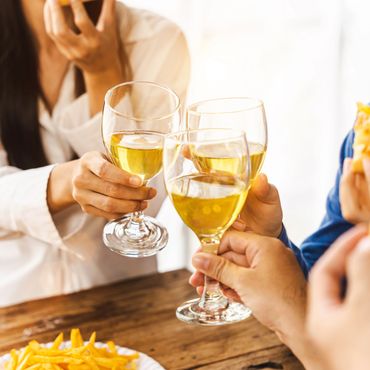 People clinking glasses with white wine over a table with fries.