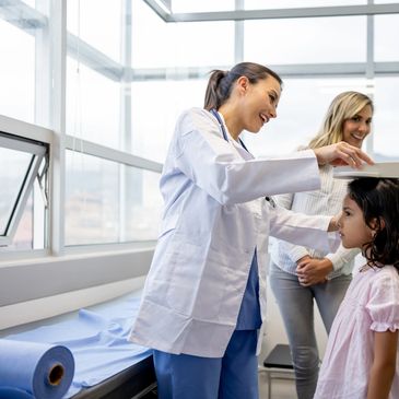 Female doctor measuring height of young girl in clinic with mother present.