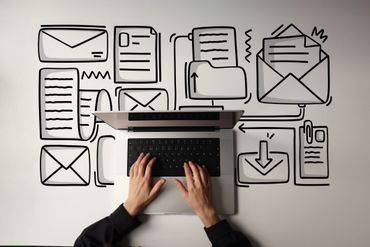 Person typing on a laptop surrounded by drawn email and document icons.