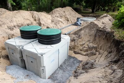Concrete septic tanks with green lids installed in a sandy excavation site.