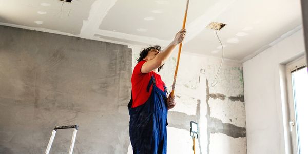 Worker applying plaster or paint to ceiling in a room under renovation.