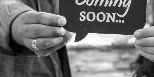 Two people holding a speech bubble sign that says 'Coming Soon...'.