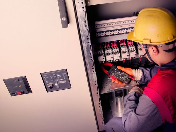 Electrician checking voltage inside an electrical panel wearing safety gear.