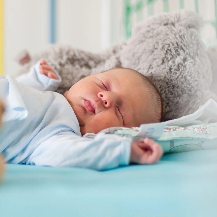 Sleeping baby in a crib with teddy bears and a blue blanket.