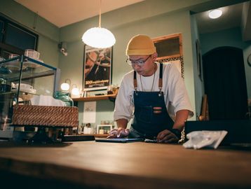 A barista in a cozy cafe wearing a yellow beanie and apron.