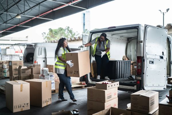 Two female warehouse or delivery workers wearing high-visibility vests and gloves 