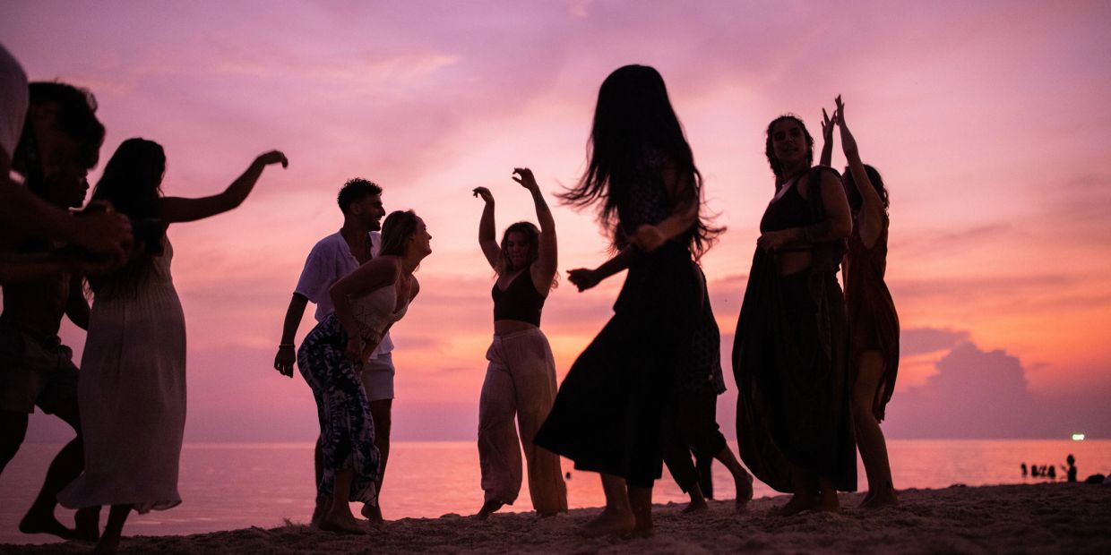 People dancing on a beach at sunset.