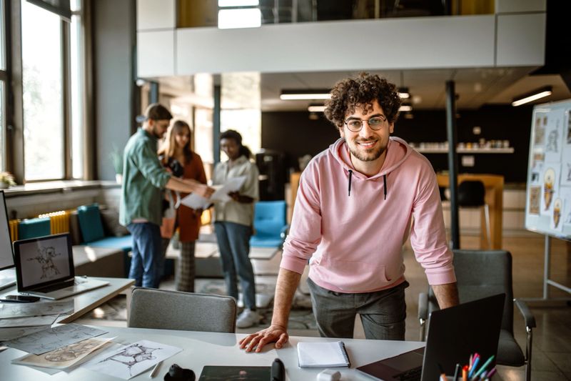 Portrait of young, smiling, confident video game designer in company studio standing in a front of his team.