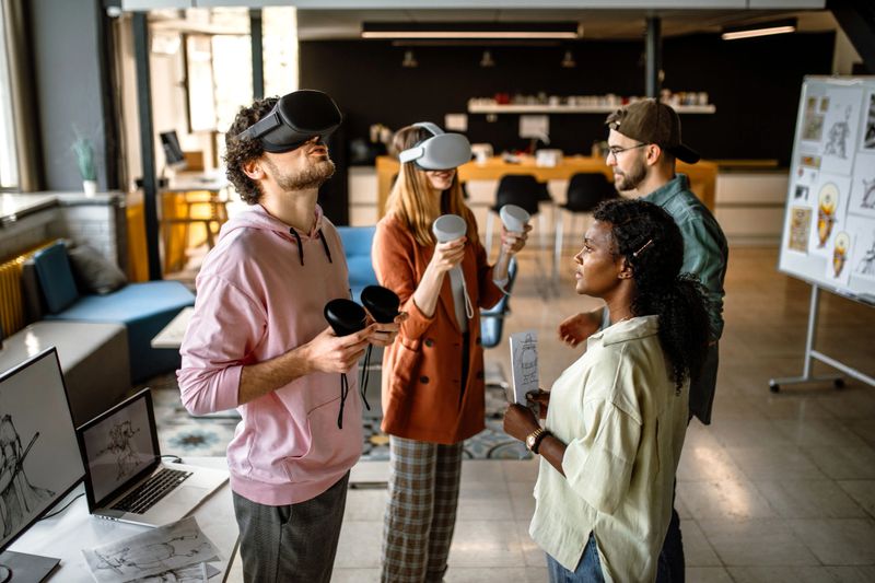 Group of colleagues in company office using virtual reality simulator headsets to test new video game they are creating.