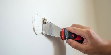 Hand applying wall filler with a putty knife.
