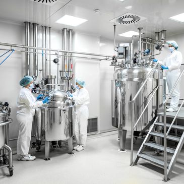 Scientists in protective gear working with stainless steel equipment in a sterile lab.