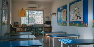Empty classroom with blue desks and colorful bulletin boards on the walls.