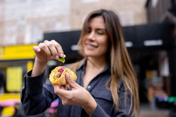 Woman squeezing lime on a taco with toppings outdoors.