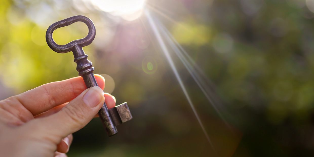 Hand holding an old-fashioned key with bright sunlight in the background.