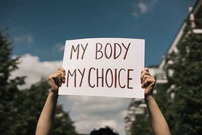 Person holding a sign saying 'My Body My Choice' outdoors.
