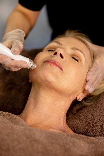 Woman receiving a facial treatment with a handheld device.