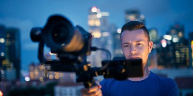 Man filming with professional camera outdoors at dusk.