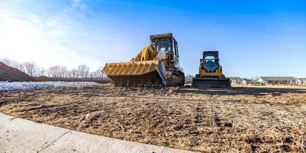 Two bulldozers parked on a cleared construction site under a bright blue sky.