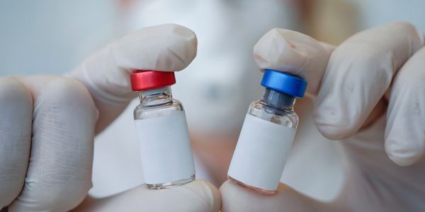 Gloved hands holding two small vaccine vials with red and blue caps.