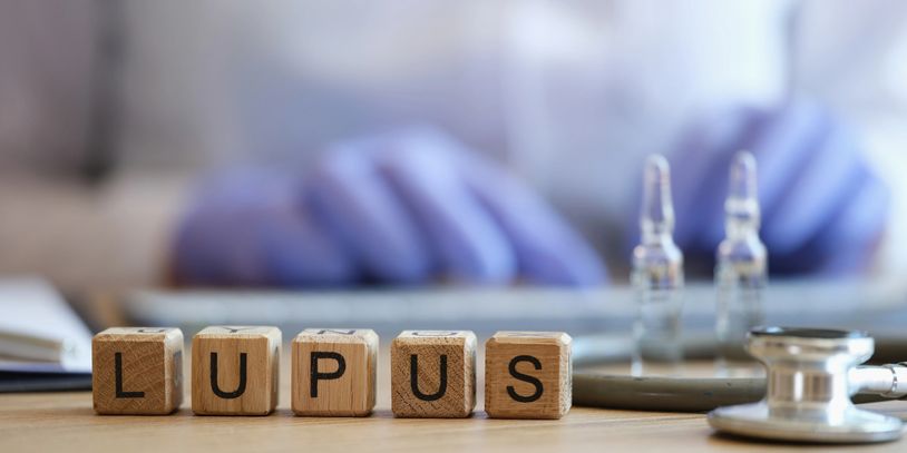 Wooden blocks spelling 'LUPUS' with medical tools in background.
