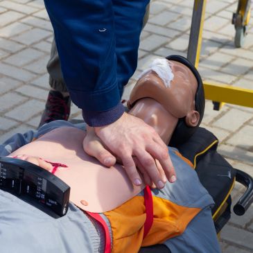Person performing CPR on a medical training mannequin outdoors.