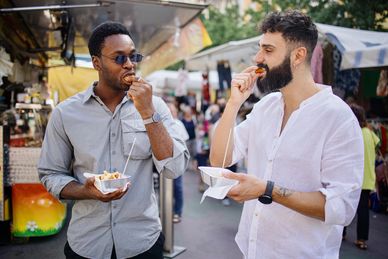 Two men eating street food at a market.