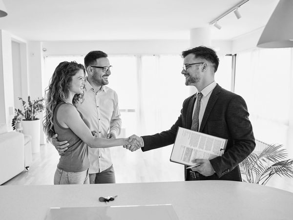 Couple shaking hands with real estate agent inside a bright home.